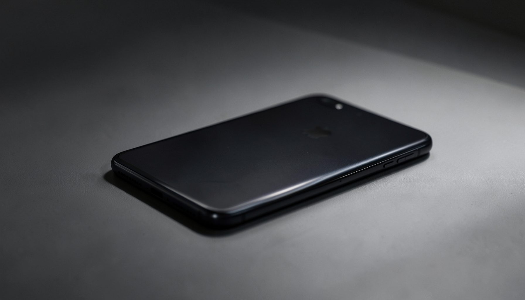A sleek smartphone with a dark titanium-like finish resting on a minimalist surface, dramatic side lighting casting soft shadows, moody and premium atmosphere.